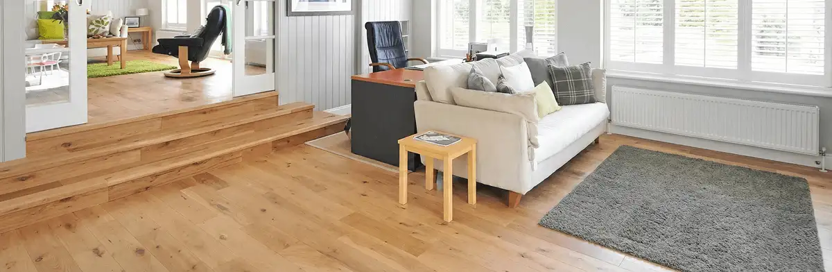 A modern living room with professionally installed laminate flooring, a beige sofa, a small side table, a gray rug, and large windows with white shutters in Jacksonville, FL